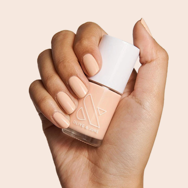 KAG nail polish by Olive and June in a neutral peachy pink shade displayed on nails against a beige background
