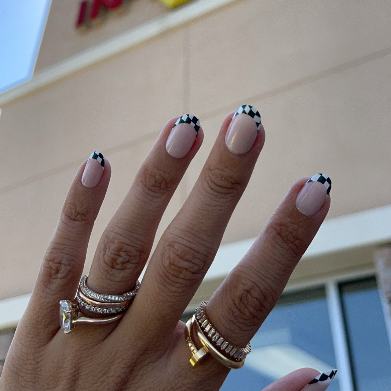 Checkerboard French - Press-On | Short | Round hand showing short round false nails with black and white checkered tips on nude base