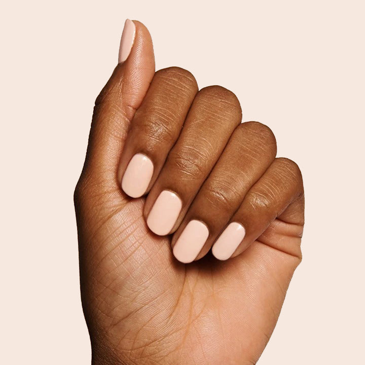Hand with neutral peachy pink KAG nail polish on nails against a soft beige background for a polished mani