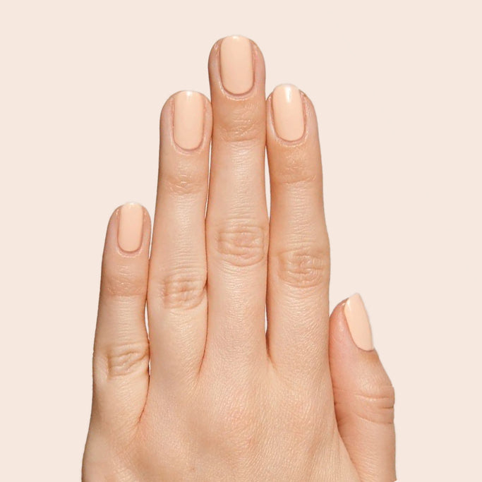 Hand with neatly painted nails in neutral peachy pink KAG polish against a light beige background for a fresh mani