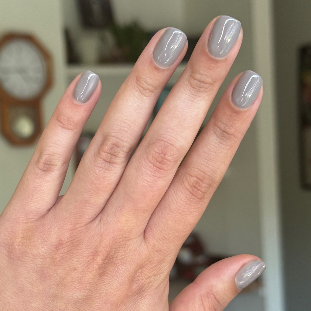 Hand with short nails painted in glossy AW - Gel warm toned grey polish for a smooth long-lasting manicure