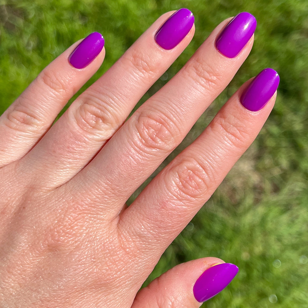 Grape Soda | Round | Short press-on nails in neon purple with a glossy finish shown on hand outdoors in natural light