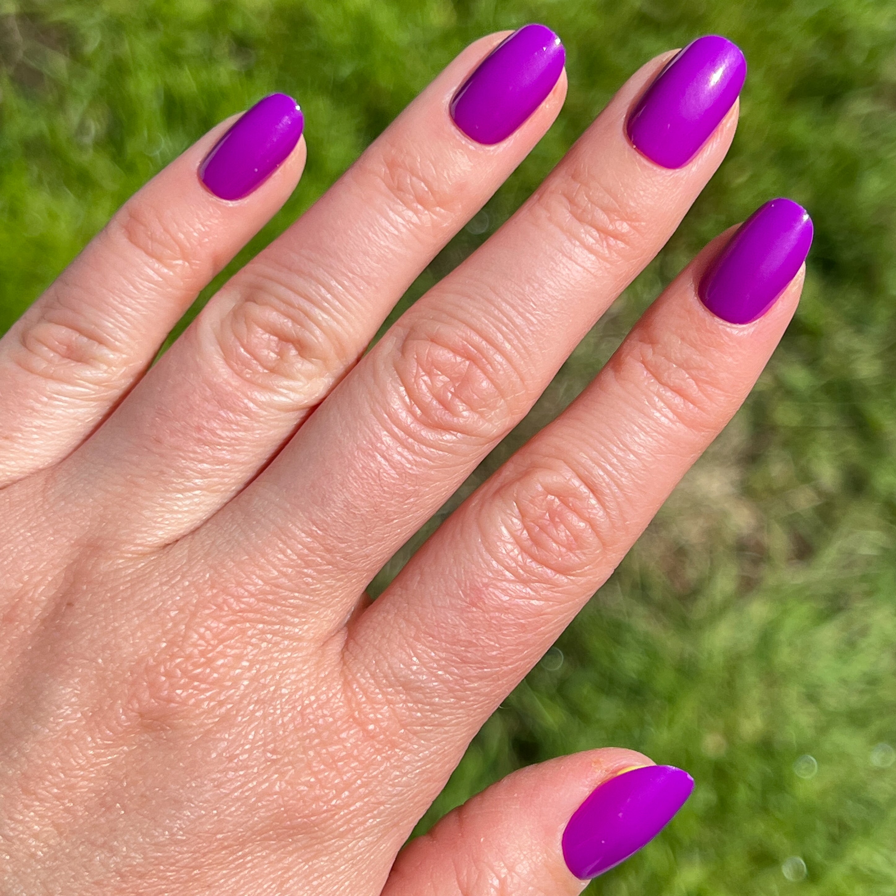 Grape Soda | Round | Short press-on nails in neon purple with a glossy finish shown on hand outdoors in natural light