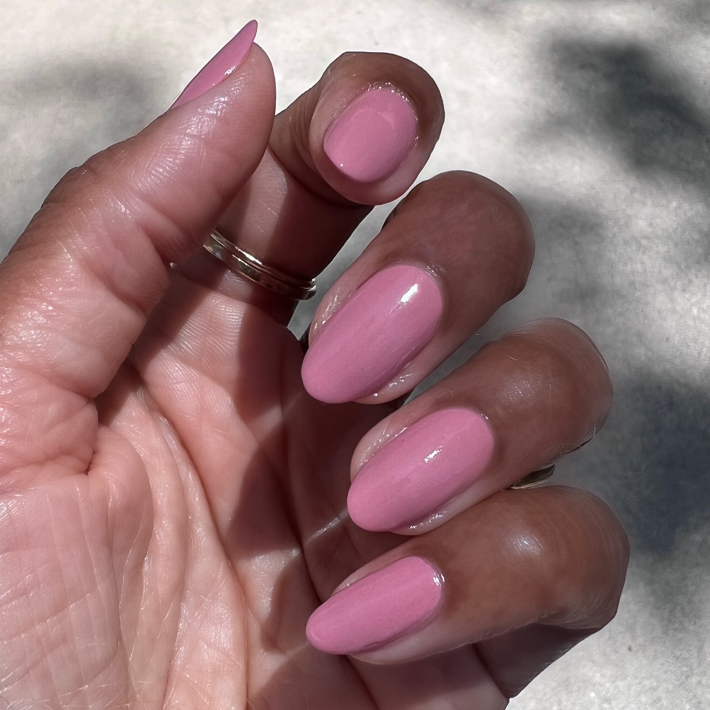 Hand with glossy nails painted in dusty rose pink Yogurt Parfait polish showing manicure in natural light outdoors