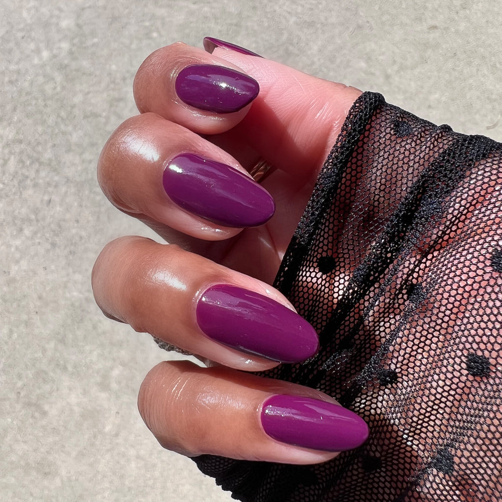 Hand with almond-shaped nails painted in glossy Plaza gel polish deep mulberry purple shade in natural light
