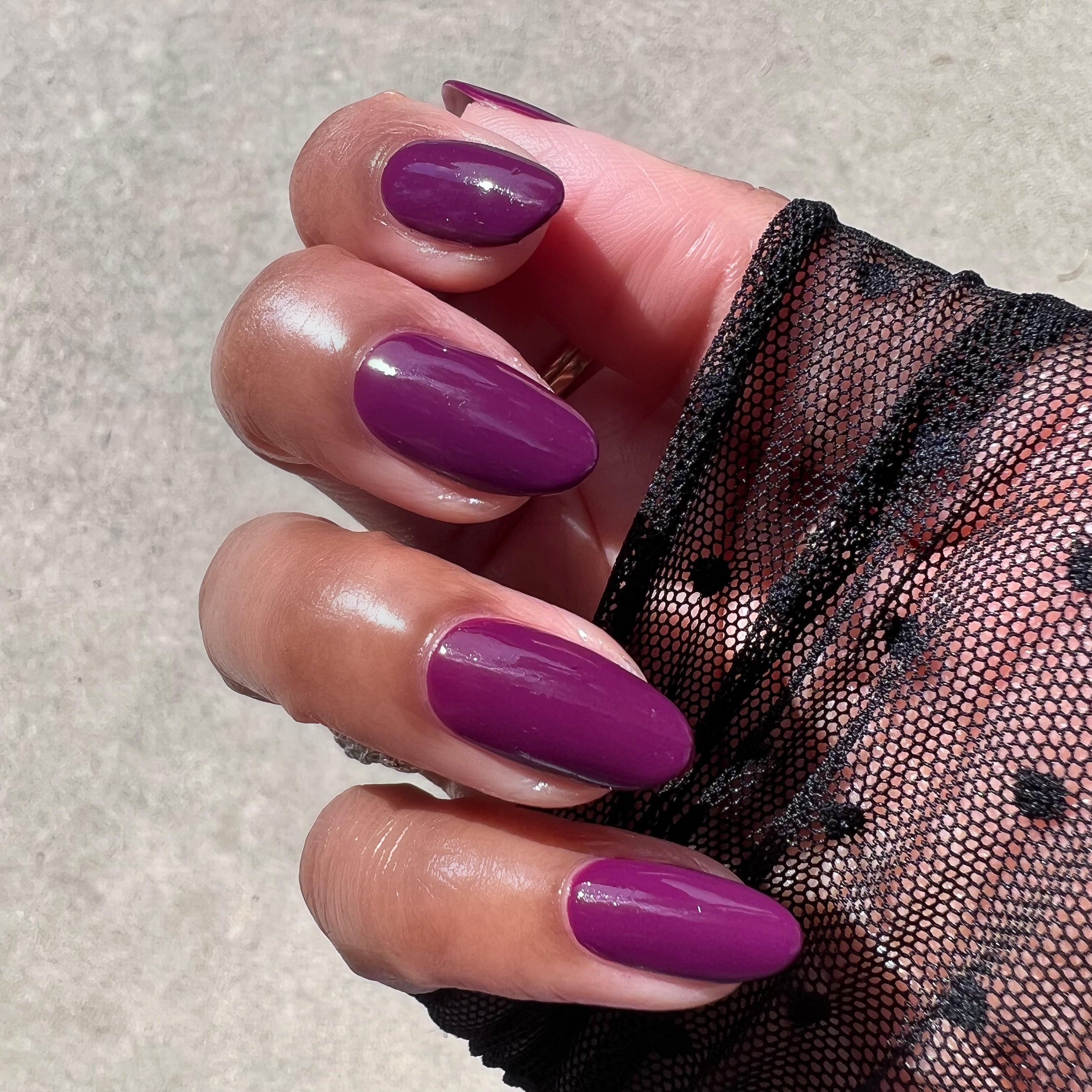 Hand with almond-shaped nails painted in glossy Plaza gel polish deep mulberry purple shade in natural light