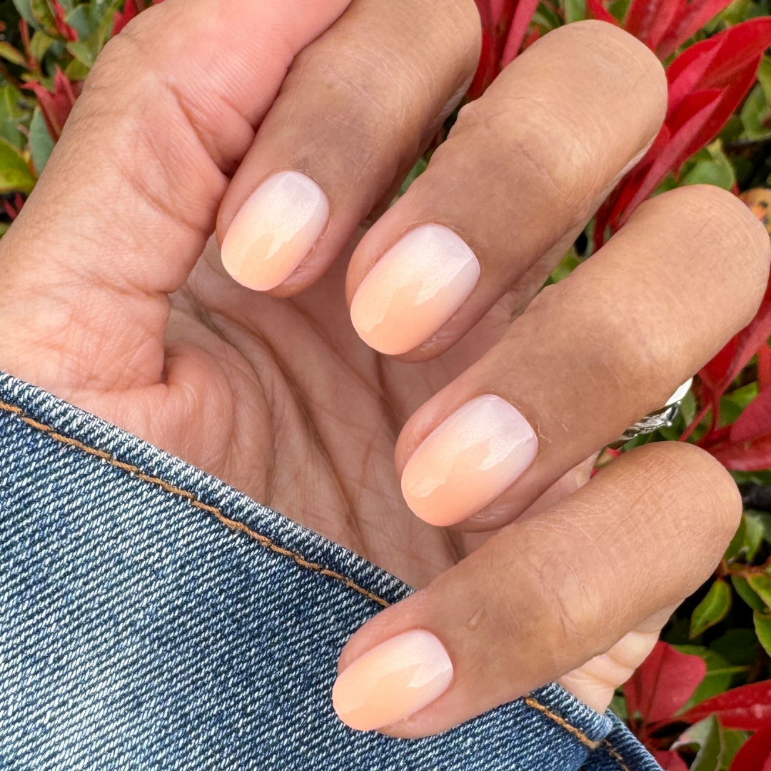 BI Syrup Gradient - Press-On | Extra Short | Round showing hand with extra short round nails in peachy pastel gradient manicure outdoors
