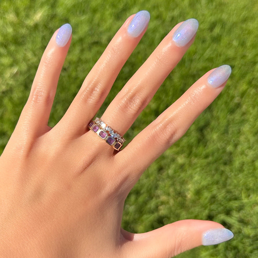 Hand with nails painted in sheer lavender-blue iridescent manicure using Friend or Anemone? polish outdoors on green grass background