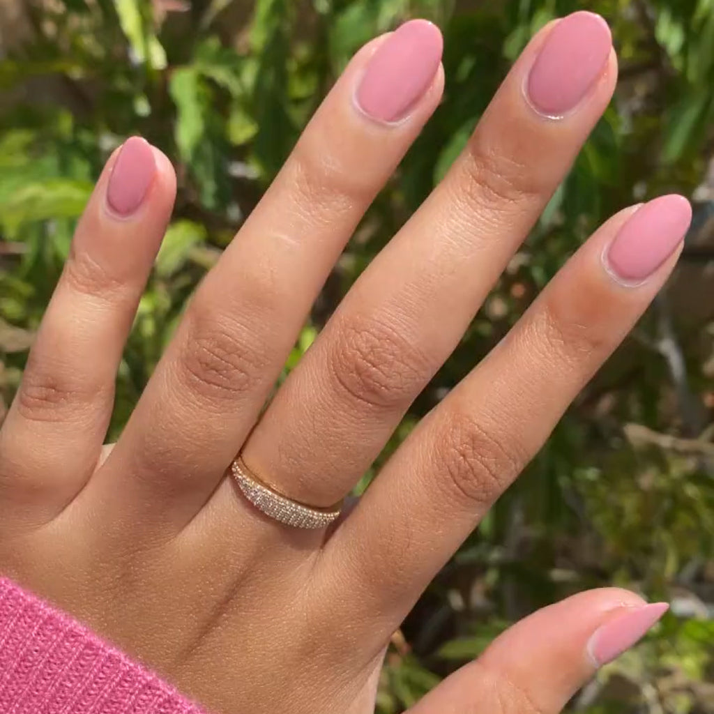 Hand with smooth nails painted in matte dusty rose pink Yogurt Parfait polish wearing diamond band ring outdoors