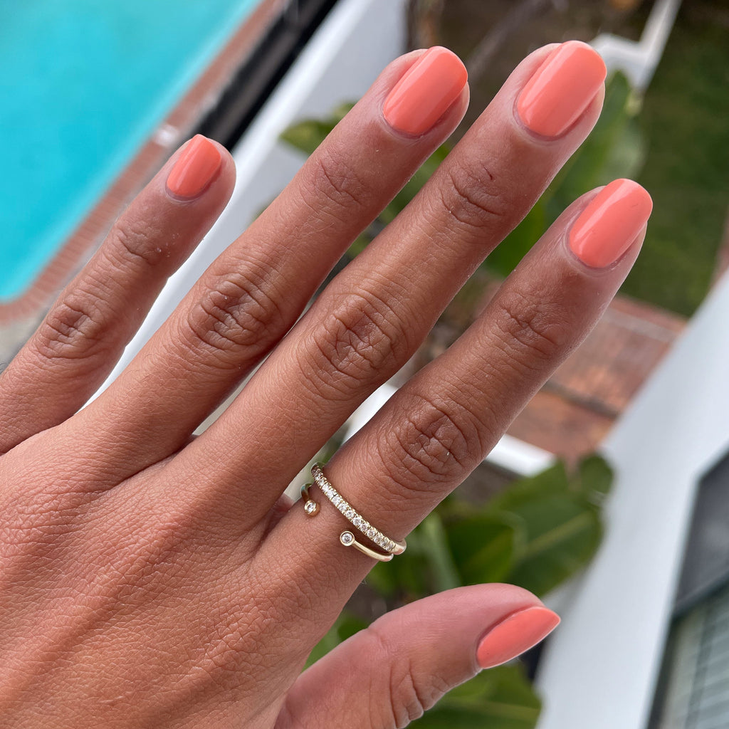 Hand with rounded nails coated in glossy Melon gel polish showing rings near poolside on a sunny day