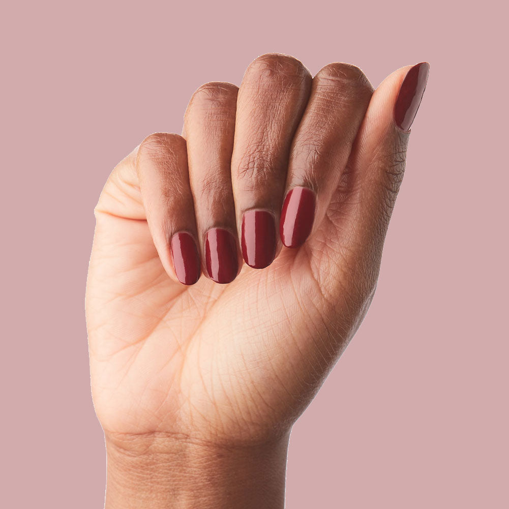Hand with medium-length nails polished in deep brick red Cozy Up nail polish for an elegant manicure look