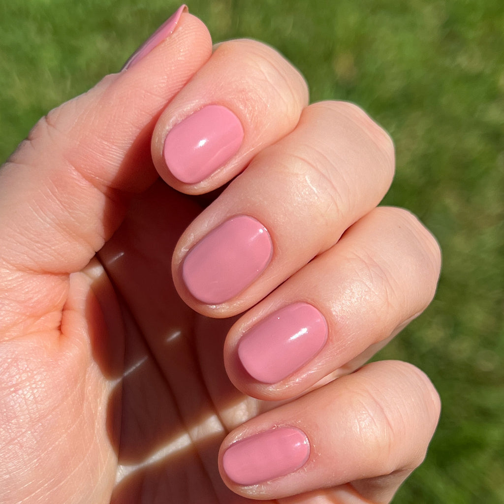 Hand with short nails painted in glossy Yogurt Parfait dusty rose polish for manicure outdoors in sunlight