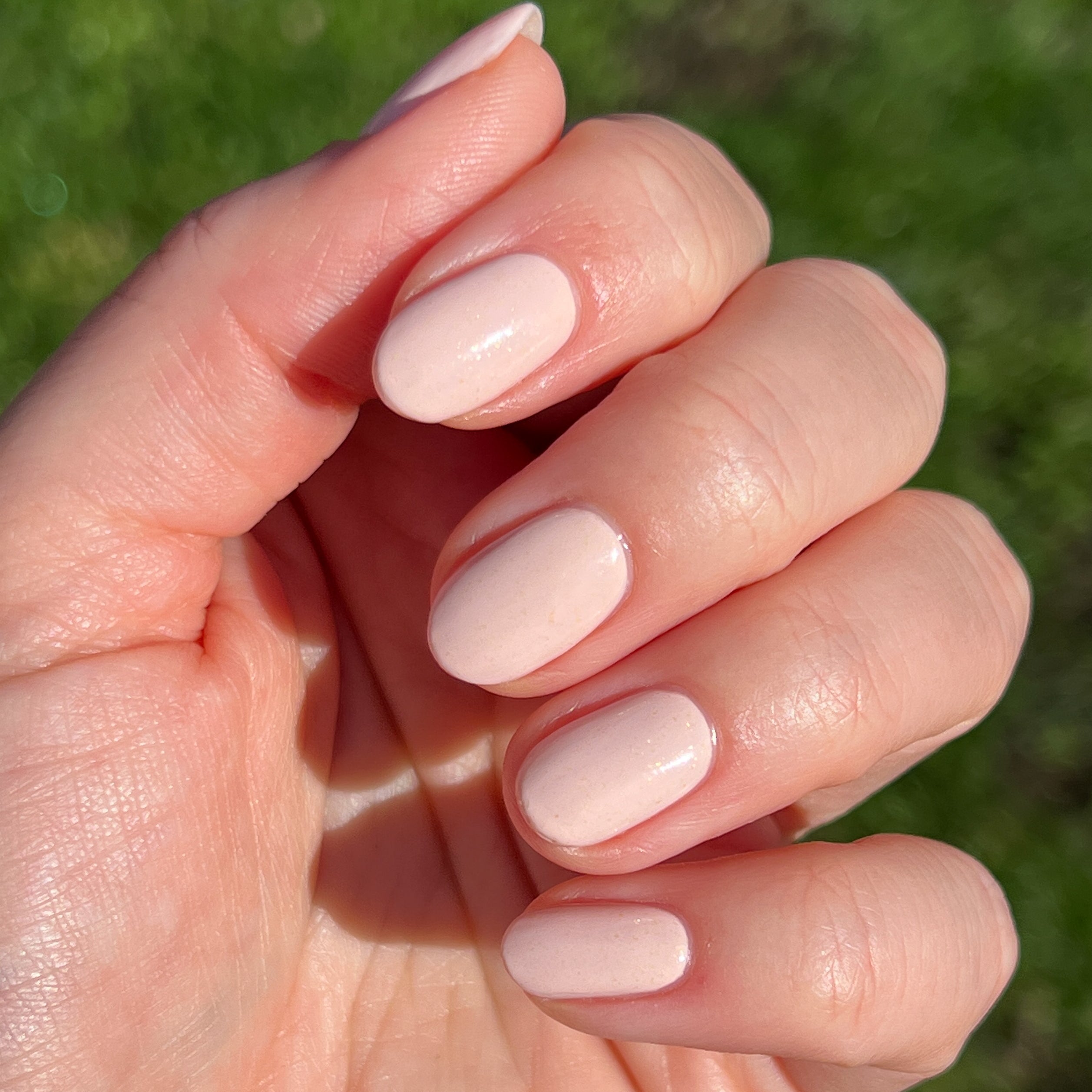 Hand with short rounded nails painted in shimmery neutral beige using cold foam pls nail polish for a natural mani