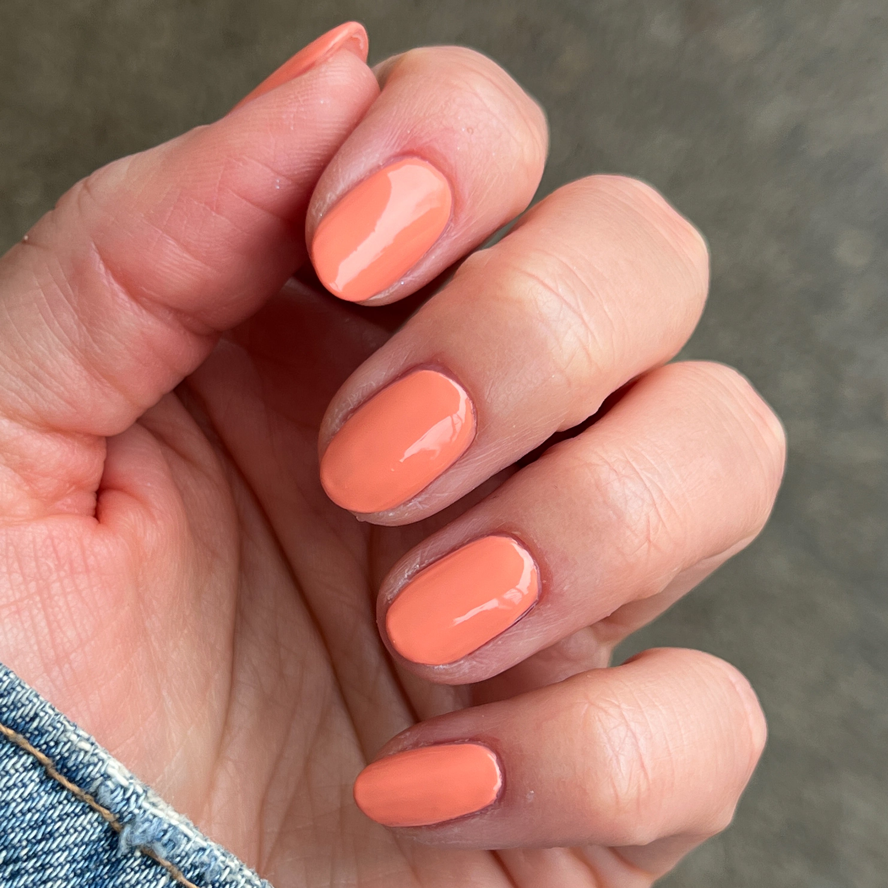 Fingernails painted with glossy Melon gel polish in vibrant cantaloupe shade on natural skin background