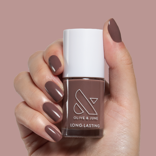 Hand holding Olive and June Clocking Out Early long-lasting gel polish bottle with matching minky brown mani on neutral background