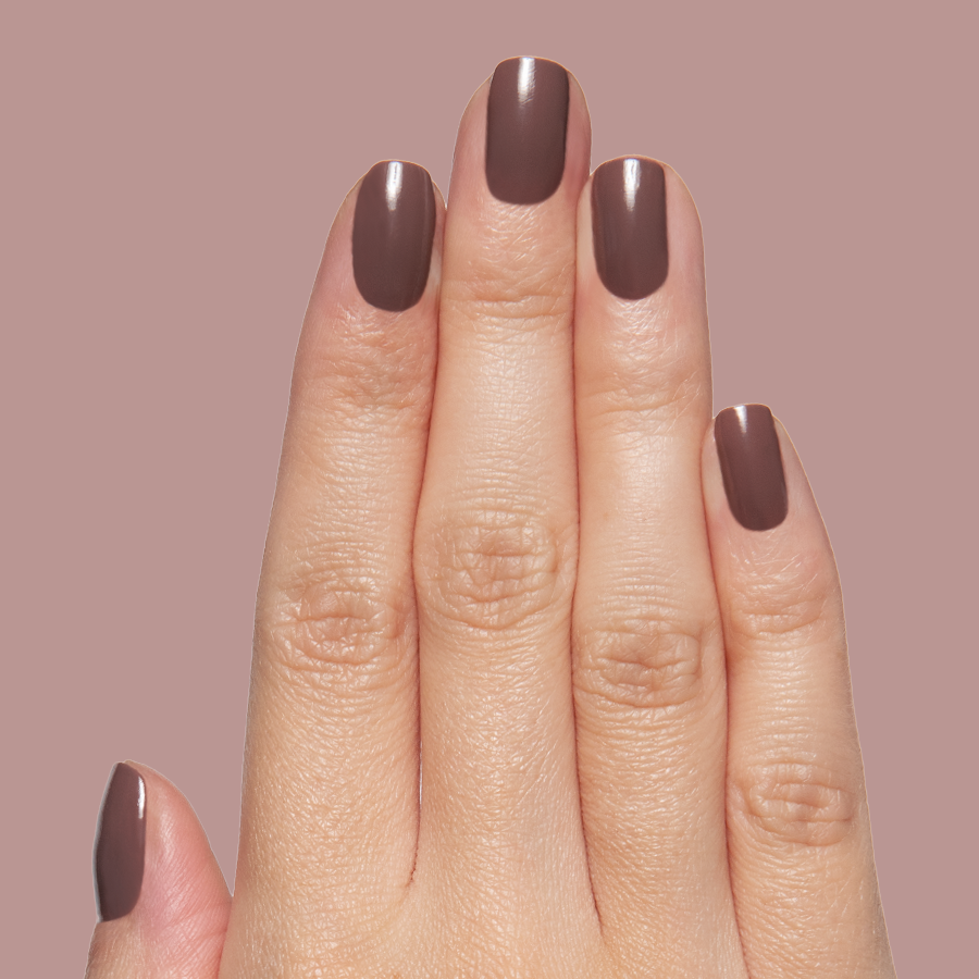 Hand with Clocking Out Early gel polish manicure in smooth neutral brown on a muted mauve background