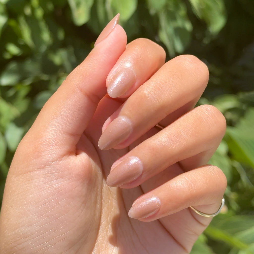 Hand with nails painted in Coconut Shimmer Gloss sheer warm chestnut polish with subtle silver shimmer outdoors