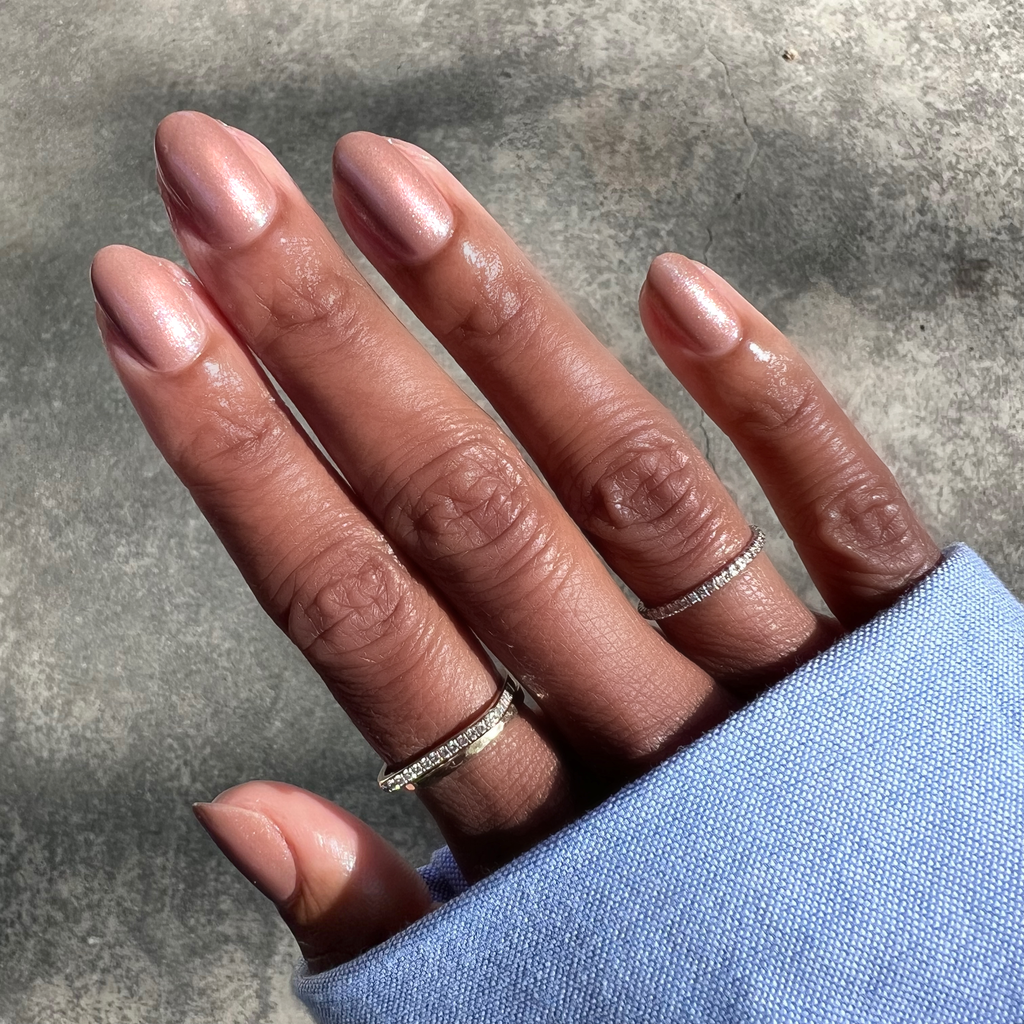 Hand with almond-shaped nails painted in Coconut Shimmer Gloss sheer warm chestnut polish with subtle silver sparkle sunlight