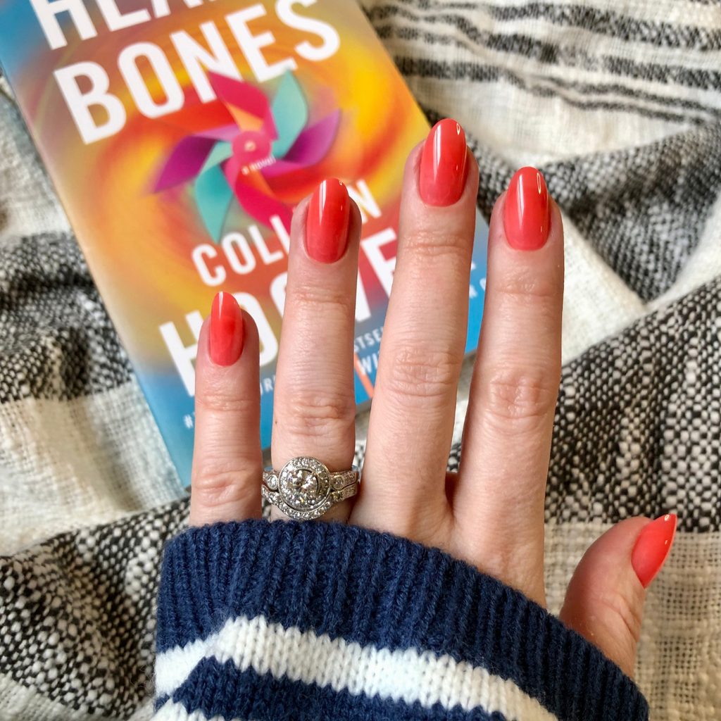 Coral Jelly - Press-On | Medium | Oval showing vibrant medium oval coral press-on nails on hand with silver rings over book cover