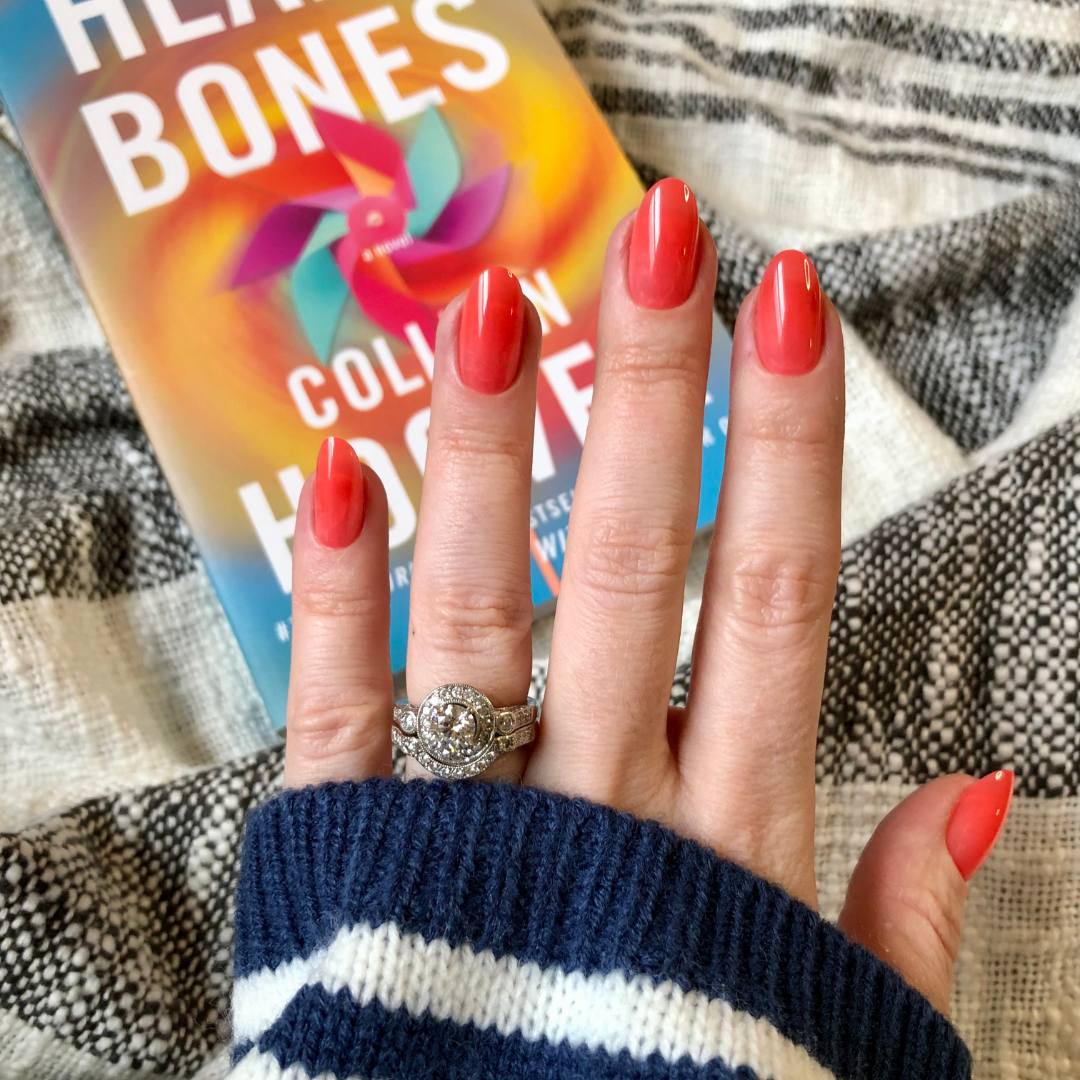 Coral Jelly - Press-On | Medium | Oval showing vibrant medium oval coral press-on nails on hand with silver rings over book cover