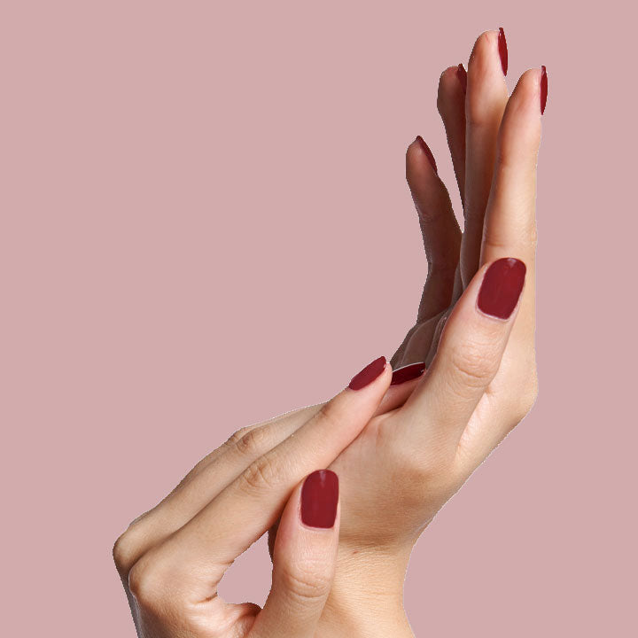 Hands with nails painted in warm brick red Cozy Up nail polish showing an elegant at-home manicure