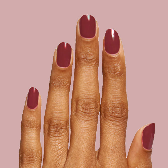 Hand with medium-length nails painted in warm brick red Cozy Up polish for a comfortable at-home manicure look