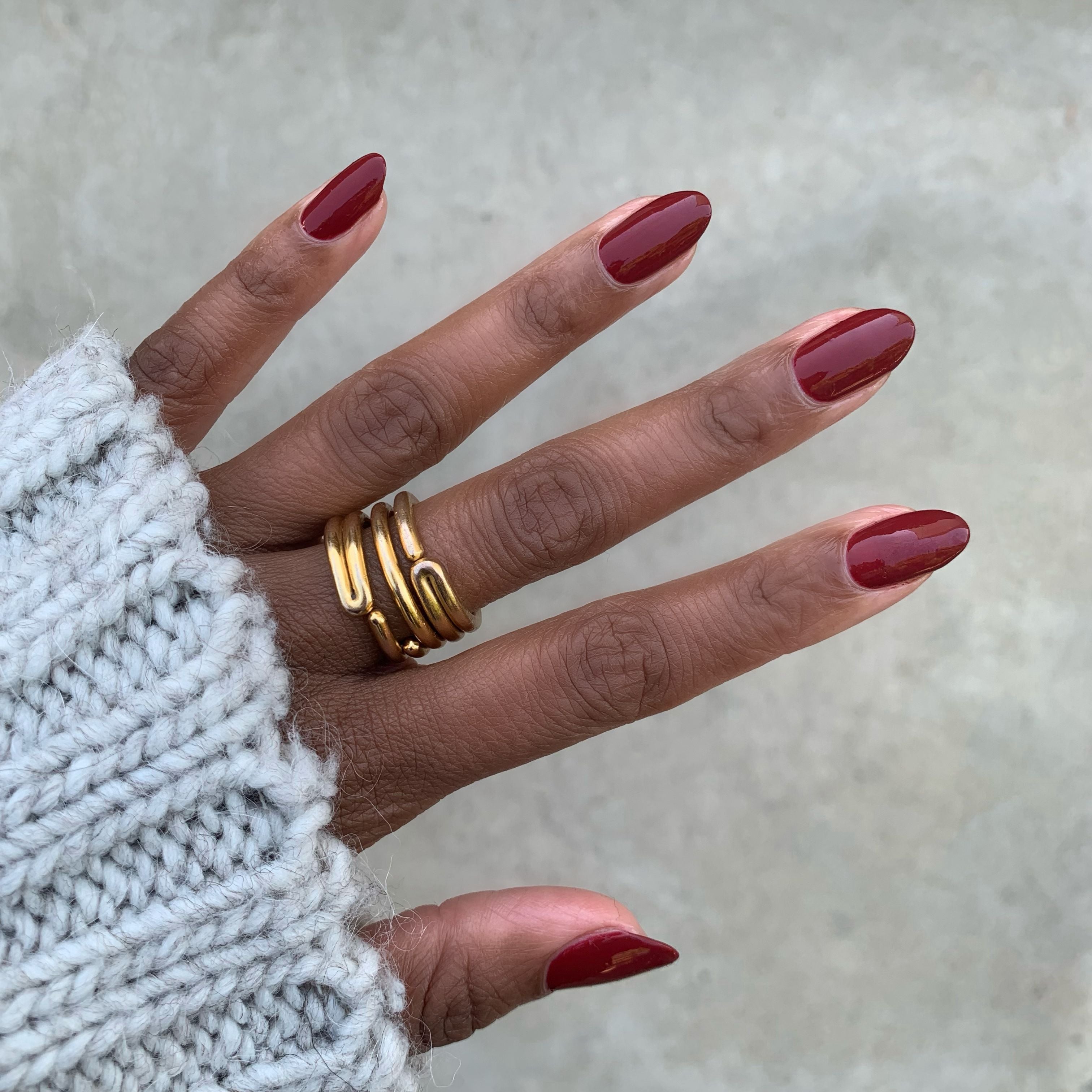 Hand with glossy Cozy Up polish in warm brick red on medium nails paired with cozy knit for at-home manicure