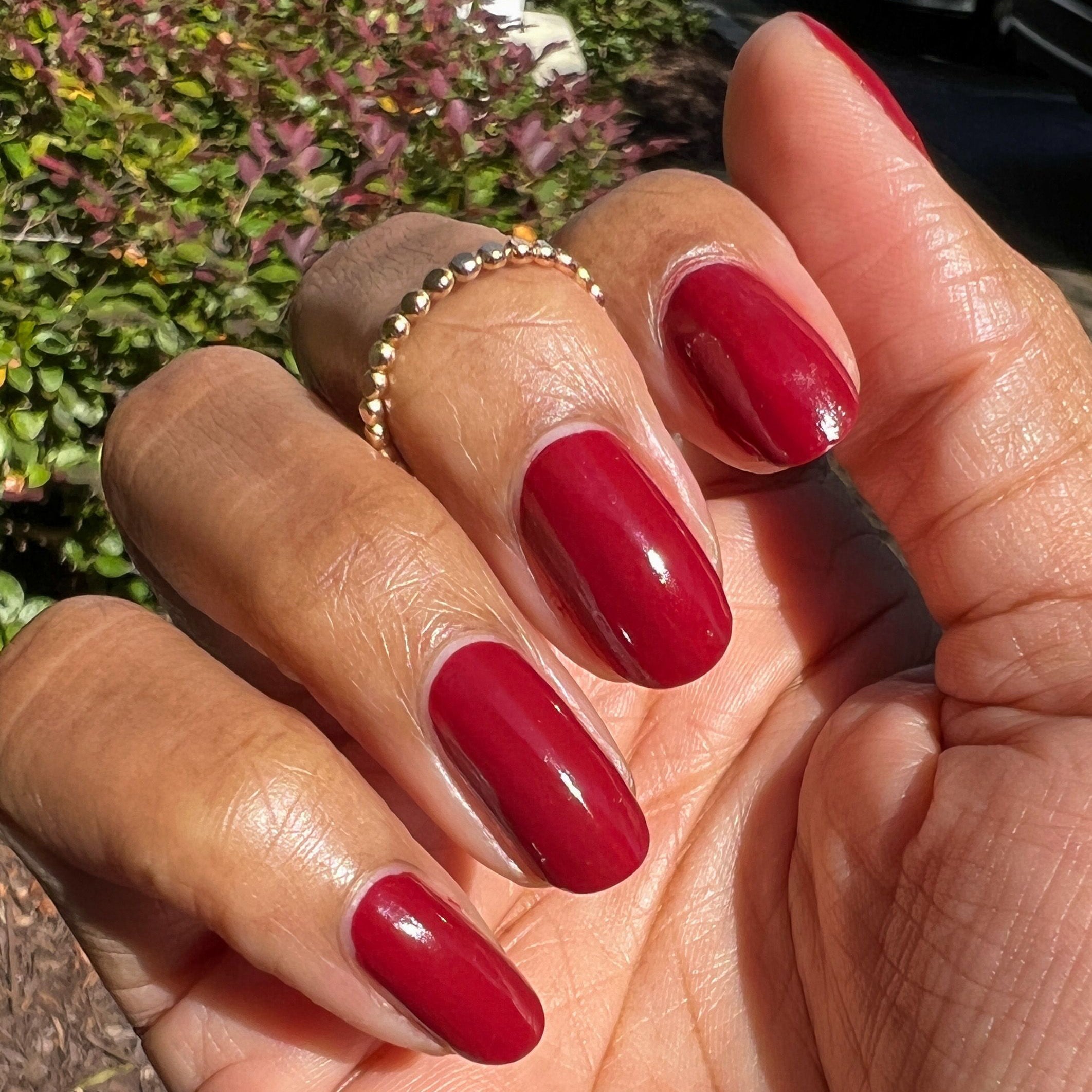 Hand with nails painted in glossy Cozy Up polish showing a rich warm brick red manicure in natural light