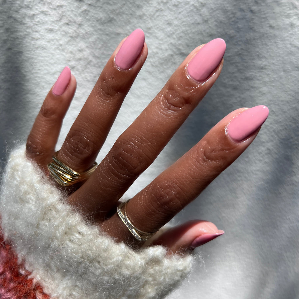 Hand with almond-shaped nails painted in smooth glossy Yogurt Parfait polish wearing gold rings and cozy sweater for manicure