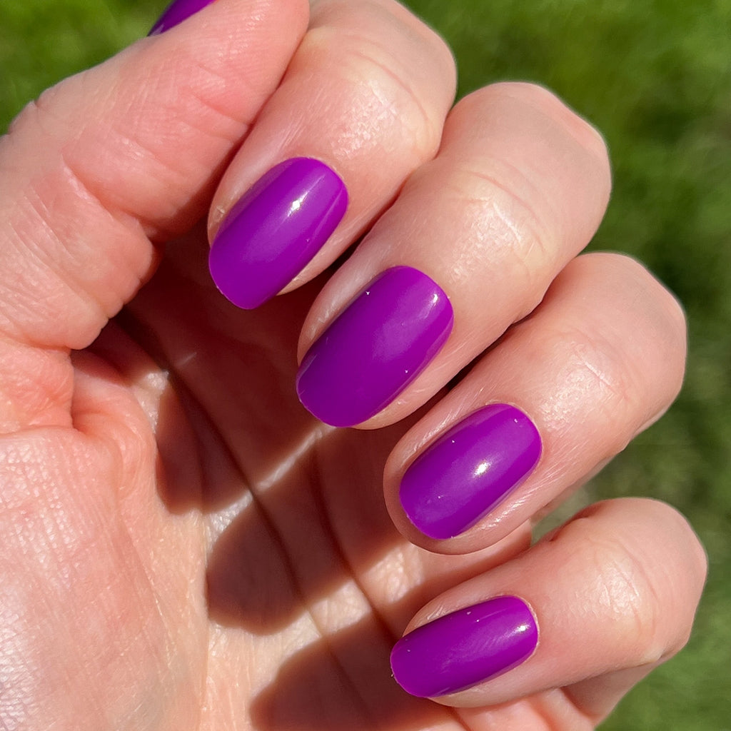 Grape Soda | Round | Short vibrant purple press-on nails in short round shape with glossy finish on hand outdoors
