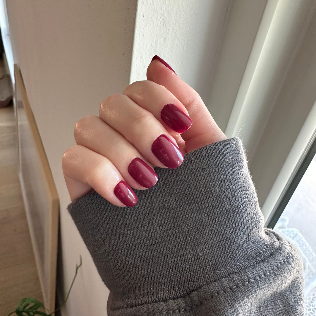 Mulberry | Extra Short | Squoval - Tab Press-On showing deep mulberry maroon press-on nails on hand in soft gray sleeve indoors