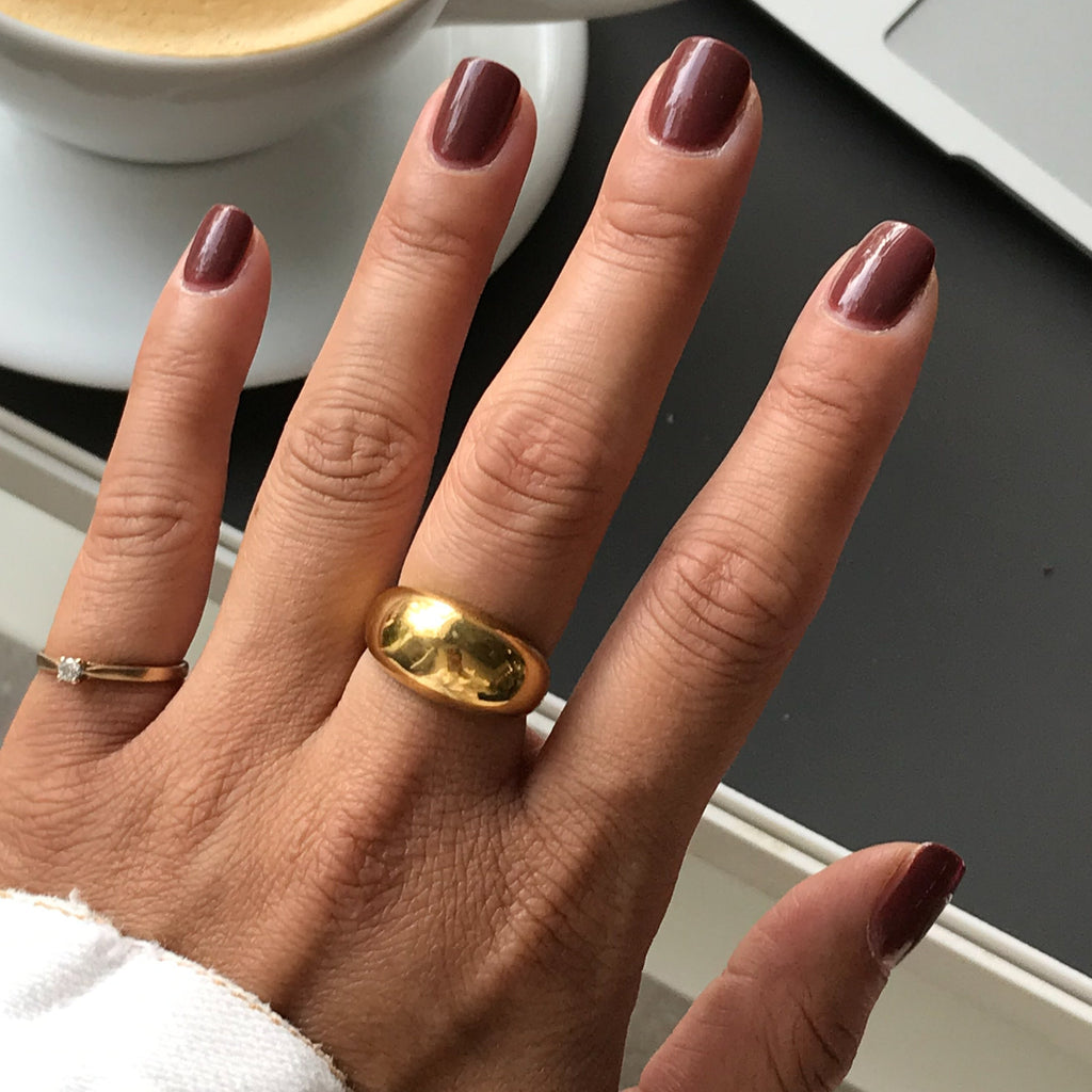 Hand with nails polished in JJ, a warm cinnamon brown gel polish, styled with gold rings for a simple mani look