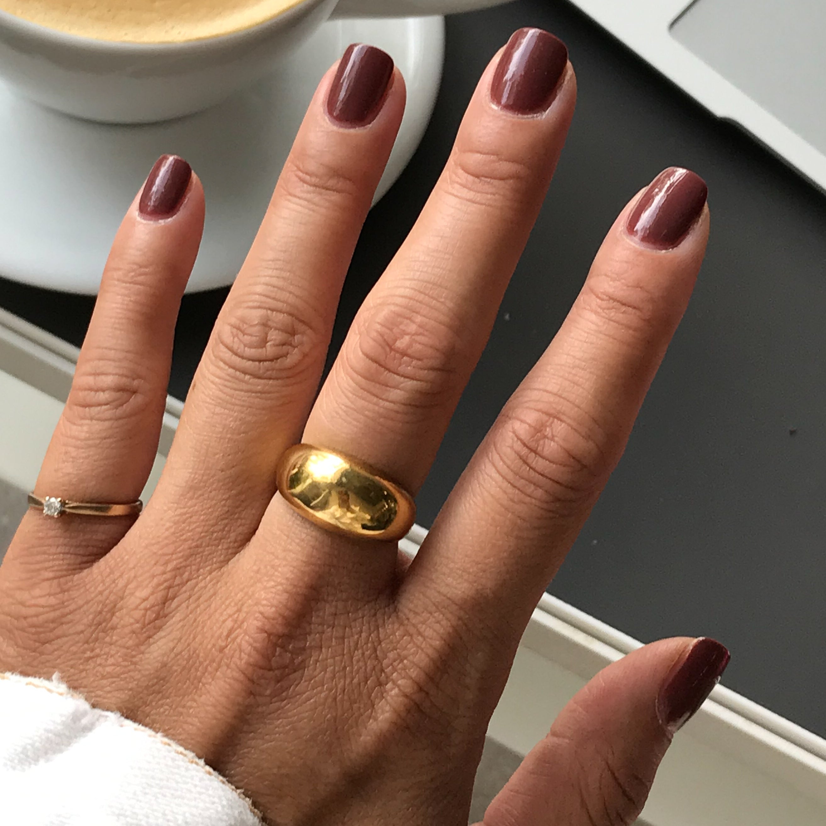 Hand with nails polished in JJ, a warm cinnamon brown gel polish, styled with gold rings for a simple mani look