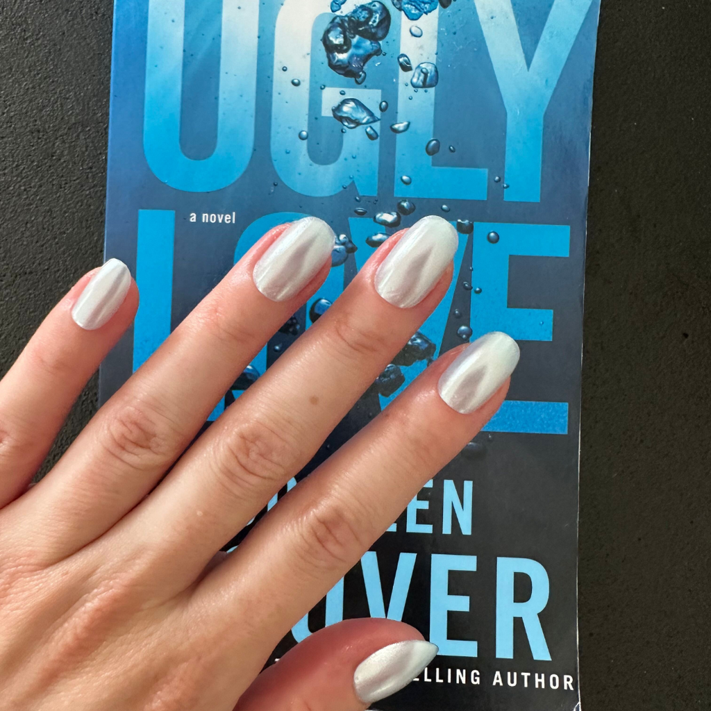 Flew In Love - Press-On | Short | Round showing pale blue chrome short round press-on false nails on hand over book cover