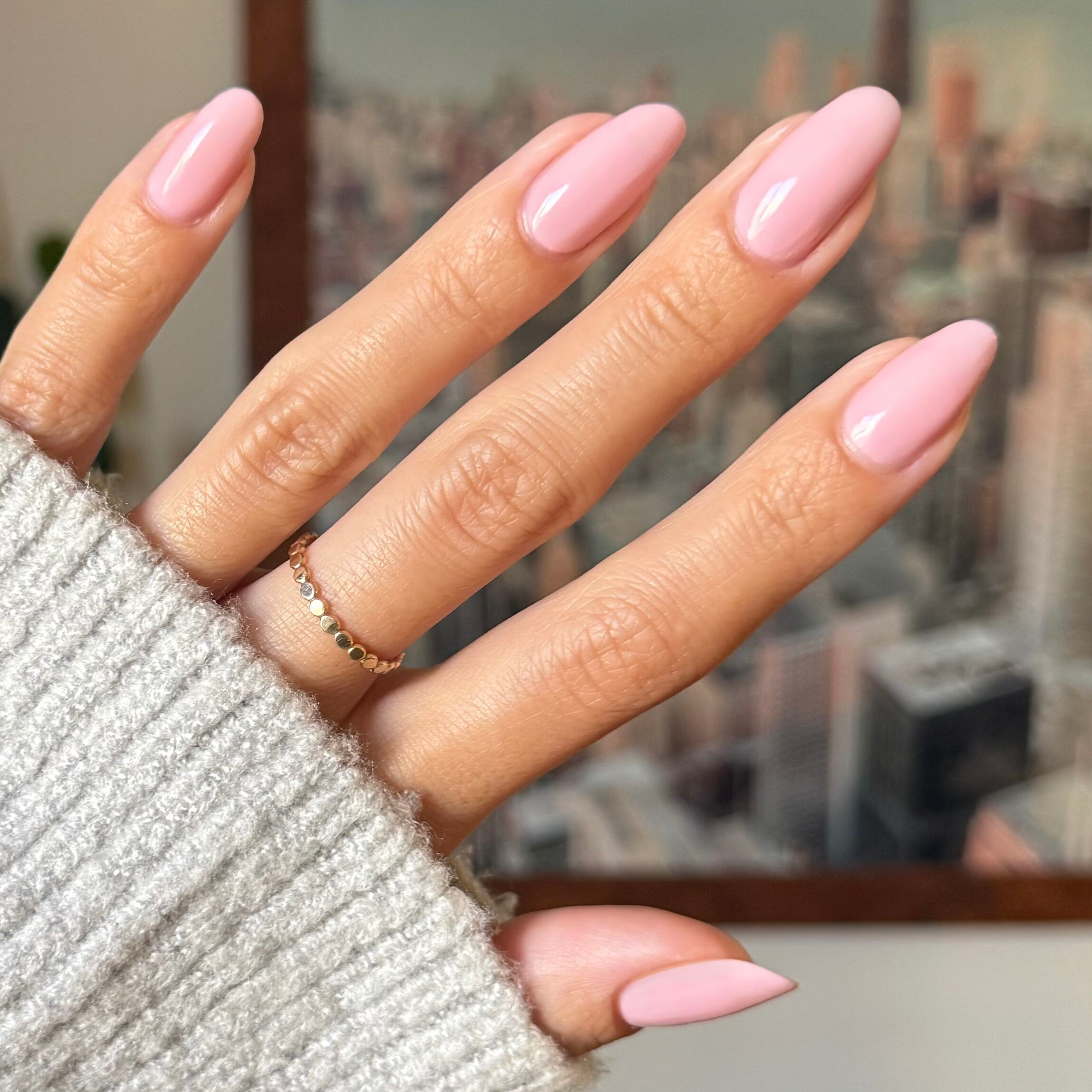 Hand with glossy milky pink manicure using Dream Job polish against a blurred cityscape background