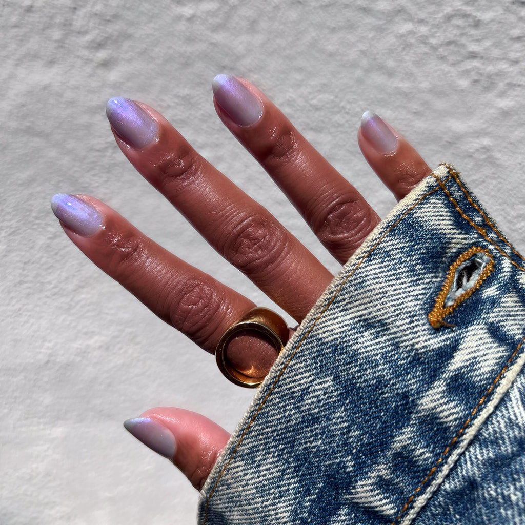 Hand with nails in sheer cool lavender-blue manicure wearing Friend or Anemone? polish and gold ring on denim sleeve
