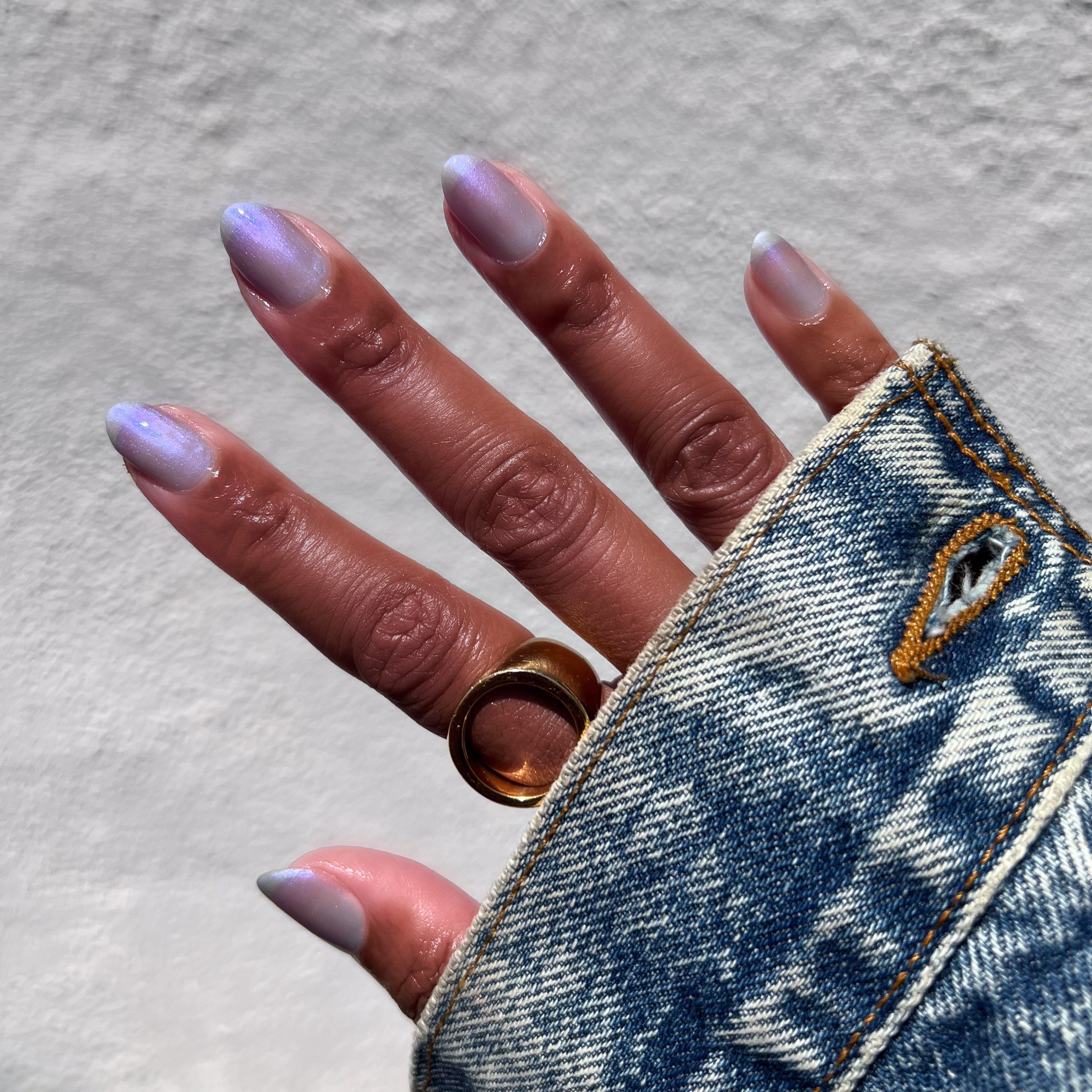 Hand with nails in sheer cool lavender-blue manicure wearing Friend or Anemone? polish and gold ring on denim sleeve