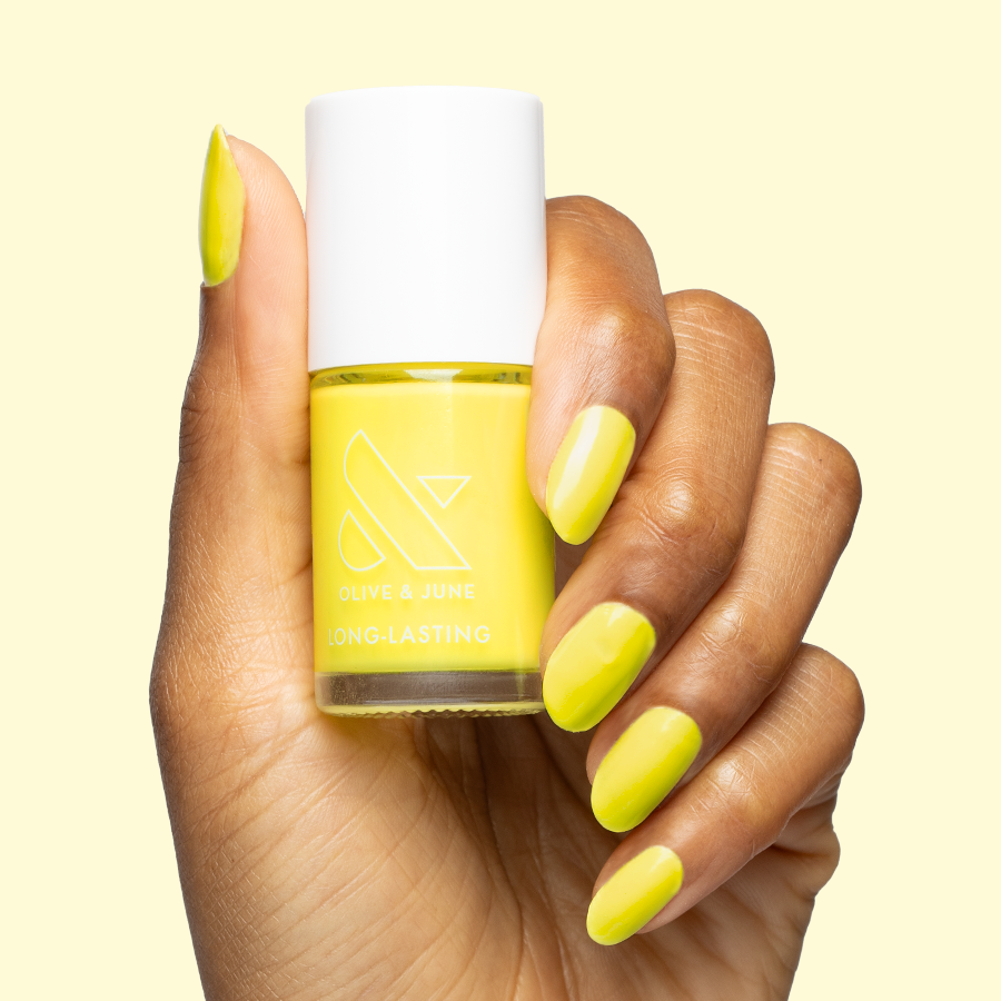 Hand holding bottle and showing nails painted in bright electric yellow Game Set Mani polish for a long-lasting mani