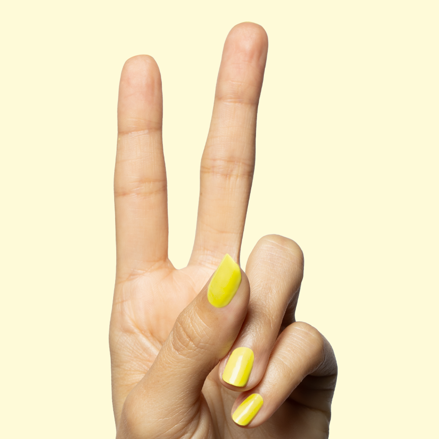 Hand showing peace sign with nails painted in bright yellow Game Set Mani for a quick-dry at-home manicure