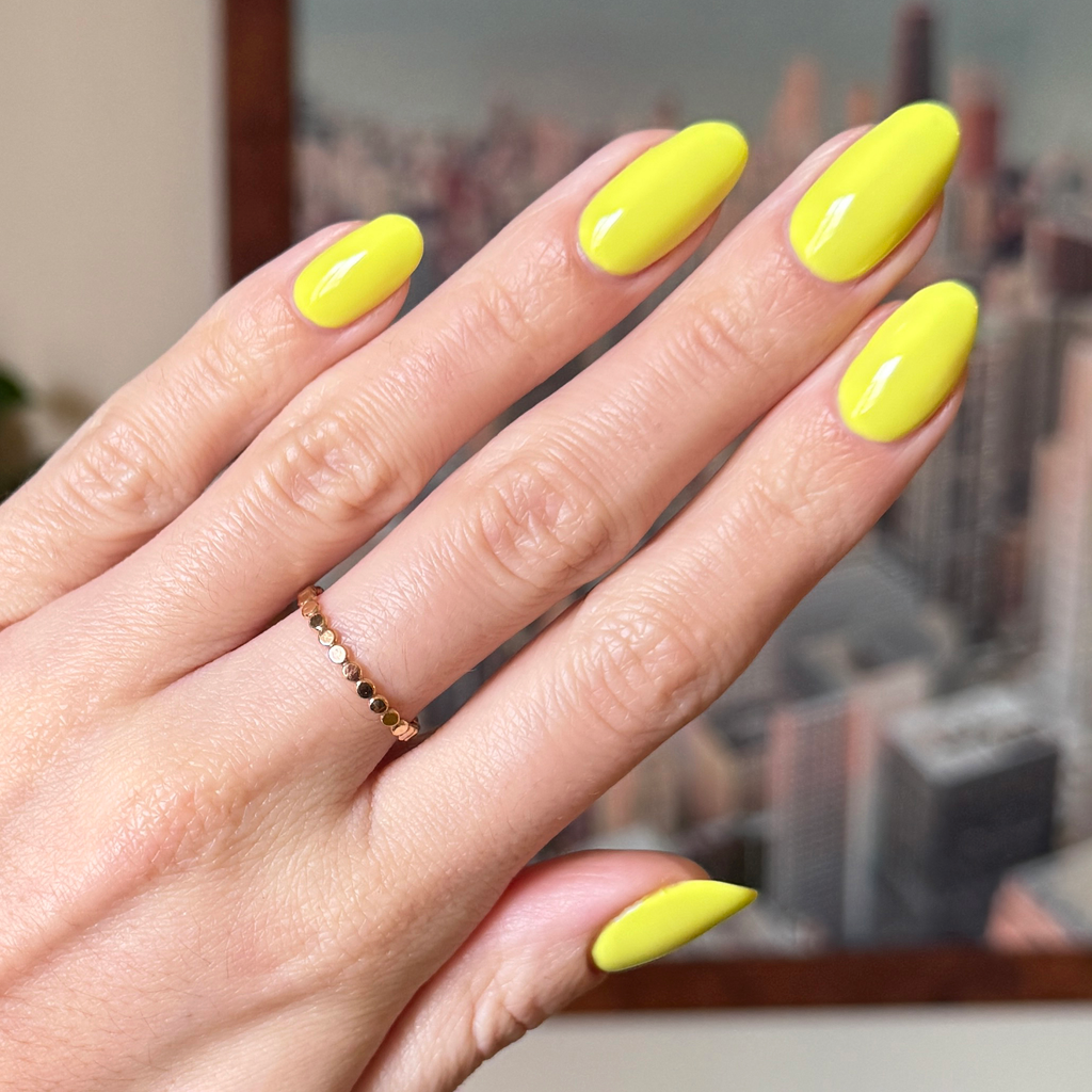 Hand with nails painted bright electric yellow Game Set Mani polish for a glossy quick-dry manicure look
