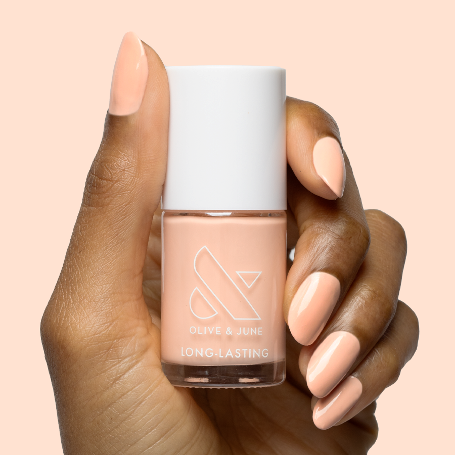 Hand with smooth nails painted in soft pastel melon shade It’s Serving Melon Cocktails nail polish by Olive and June