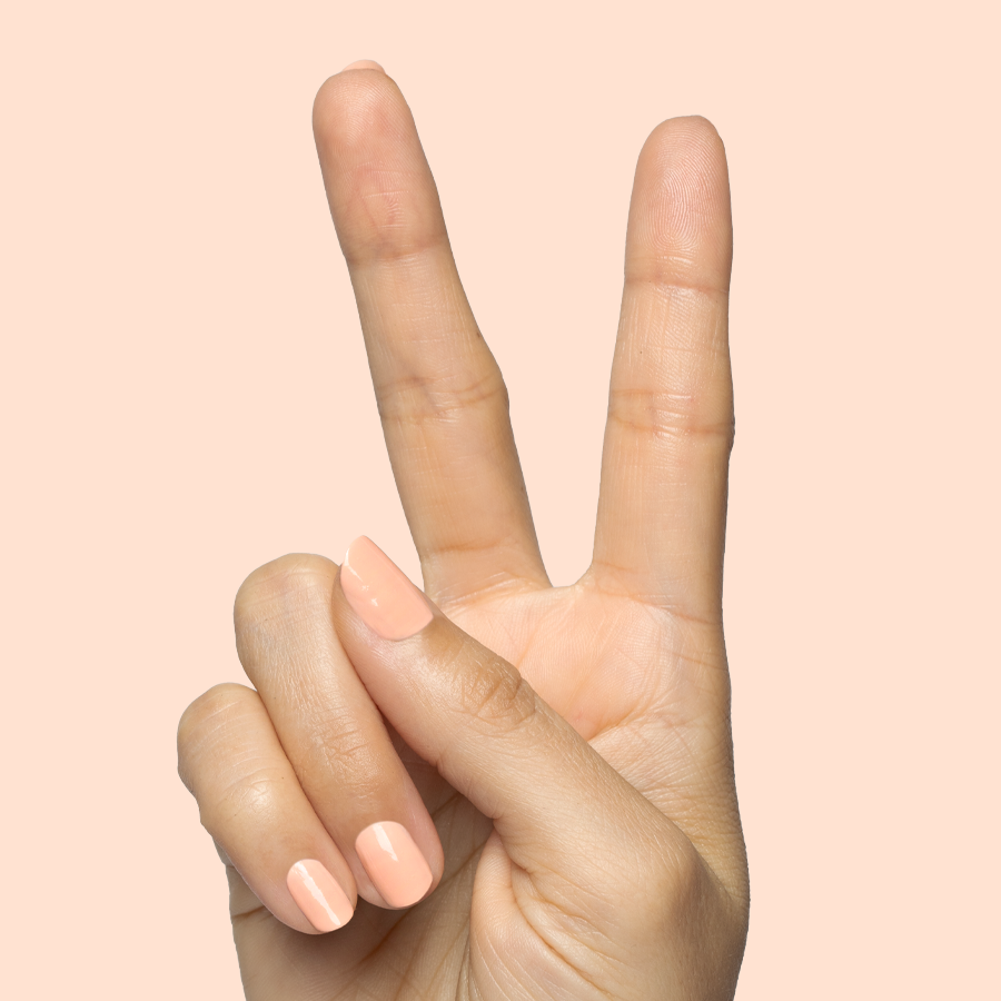 Hand with glossy nails painted in soft pastel melon shade It’s Serving Melon Cocktails for a fresh at-home mani look