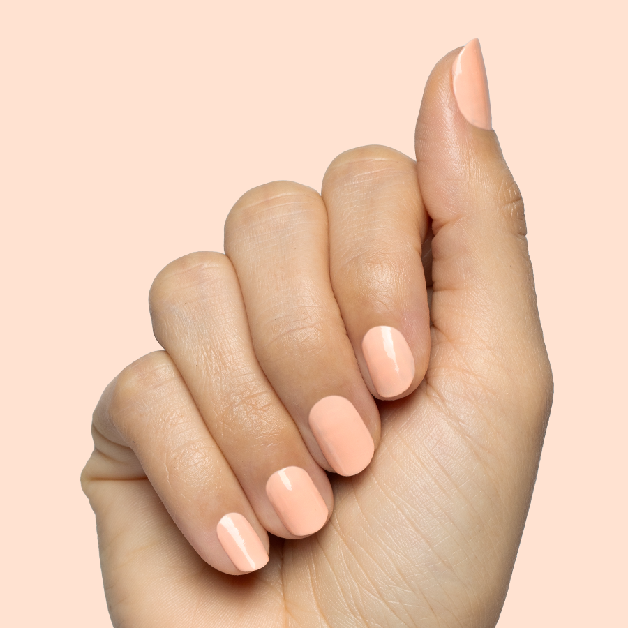 Hand with smooth nails painted in soft pastel melon shade It’s Serving Melon Cocktails for a fresh at-home manicure