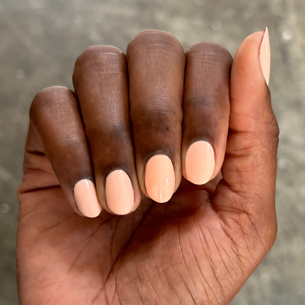 Hand with neatly shaped nails painted in soft pastel melon shade It’s Serving Melon Cocktails polish for a fresh mani