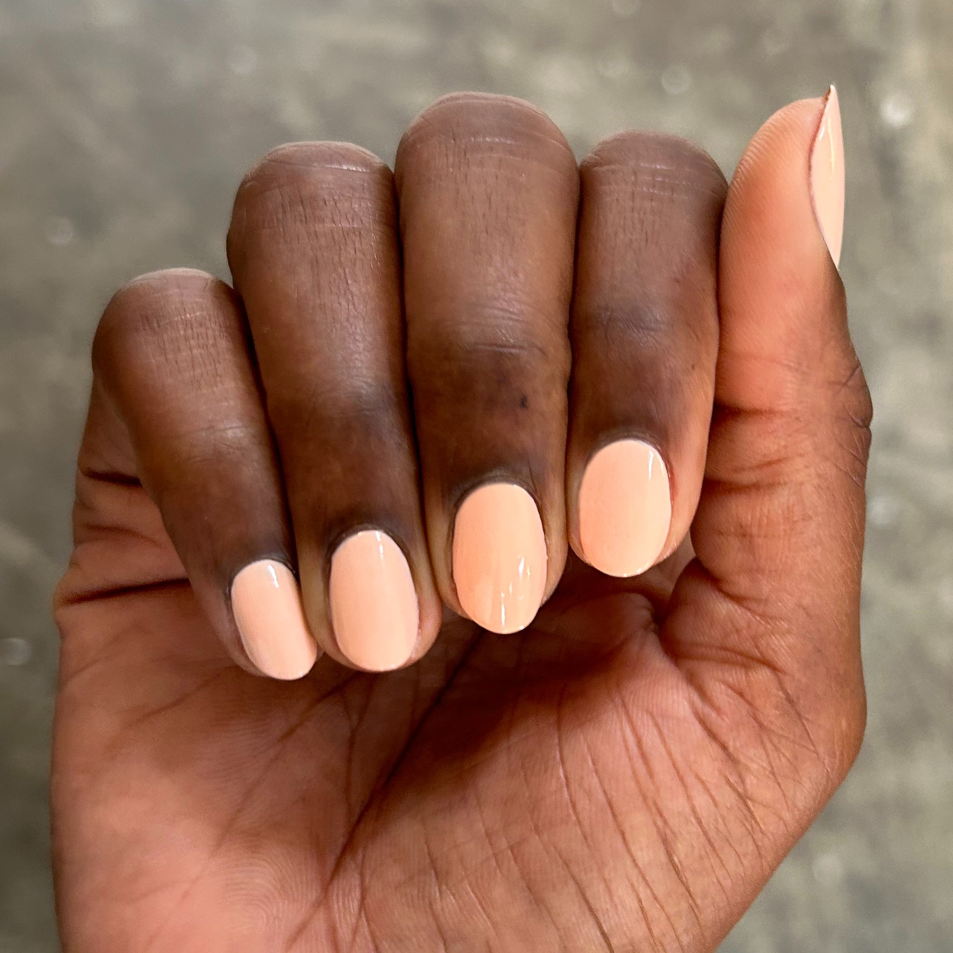 Hand with neatly shaped nails painted in soft pastel melon shade It’s Serving Melon Cocktails polish for a fresh mani