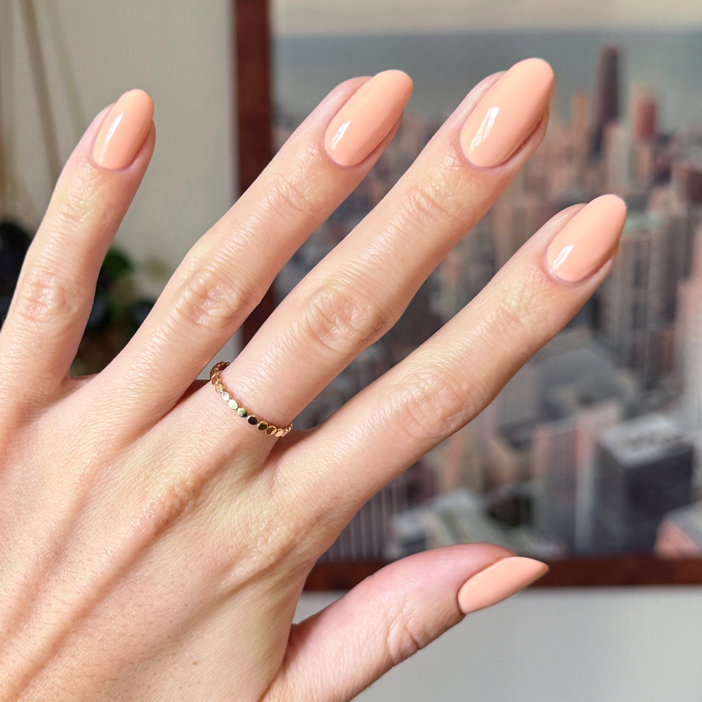 Hand with glossy nails coated in soft pastel melon shade It’s Serving Melon Cocktails for a fresh at-home manicure