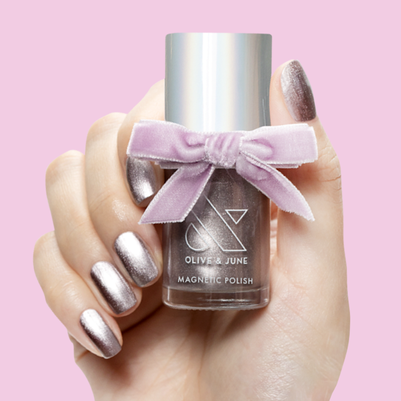 Hand holding Lavender Velvet magnetic polish bottle with shimmery frosty purple nails against soft pink background
