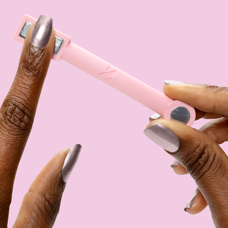 Hand holding pink magnetic tool over nails painted with Lavender Velvet frosty purple polish on a soft pink background