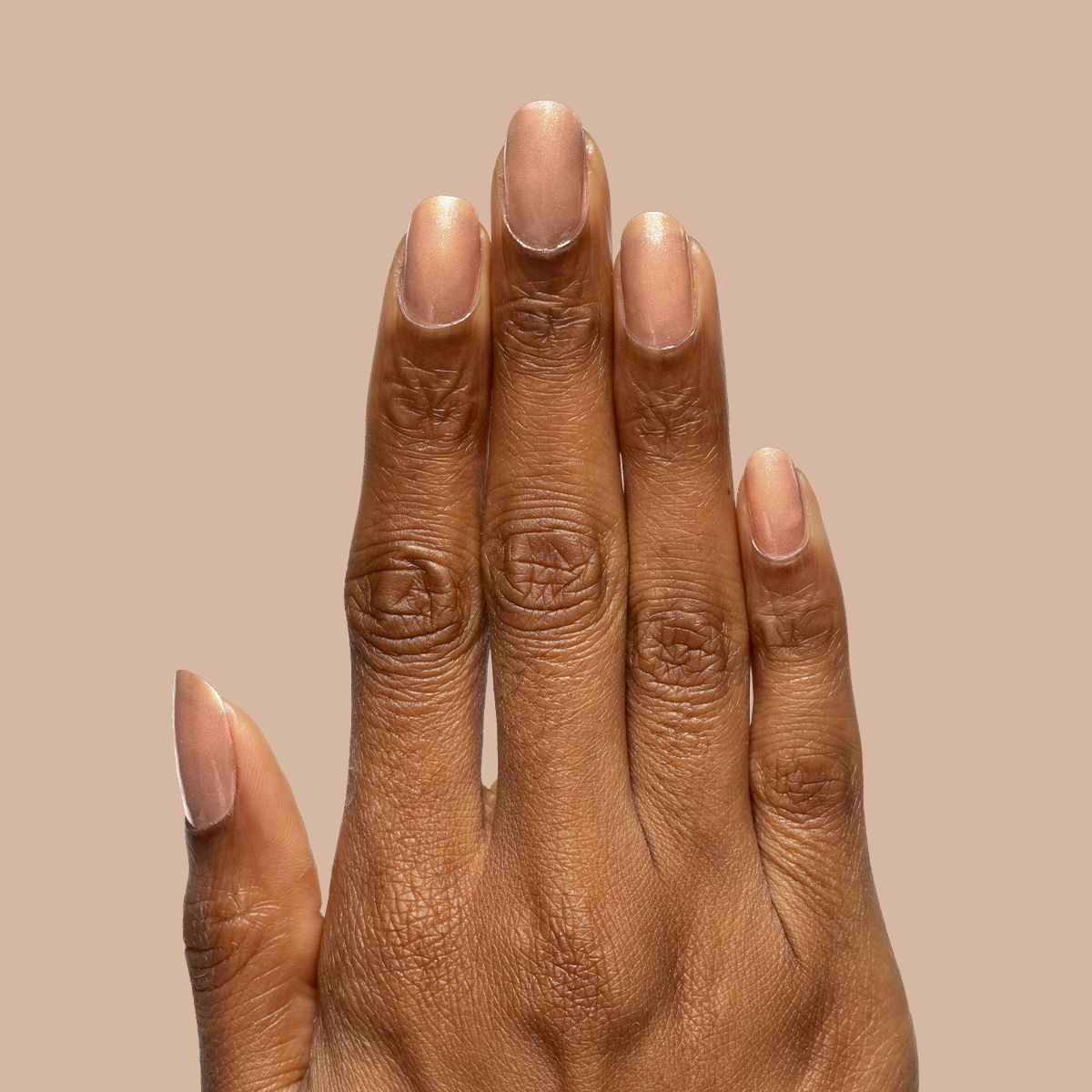 Hand with nails coated in sheer warm chestnut Coconut Shimmer Gloss gel polish on neutral beige background