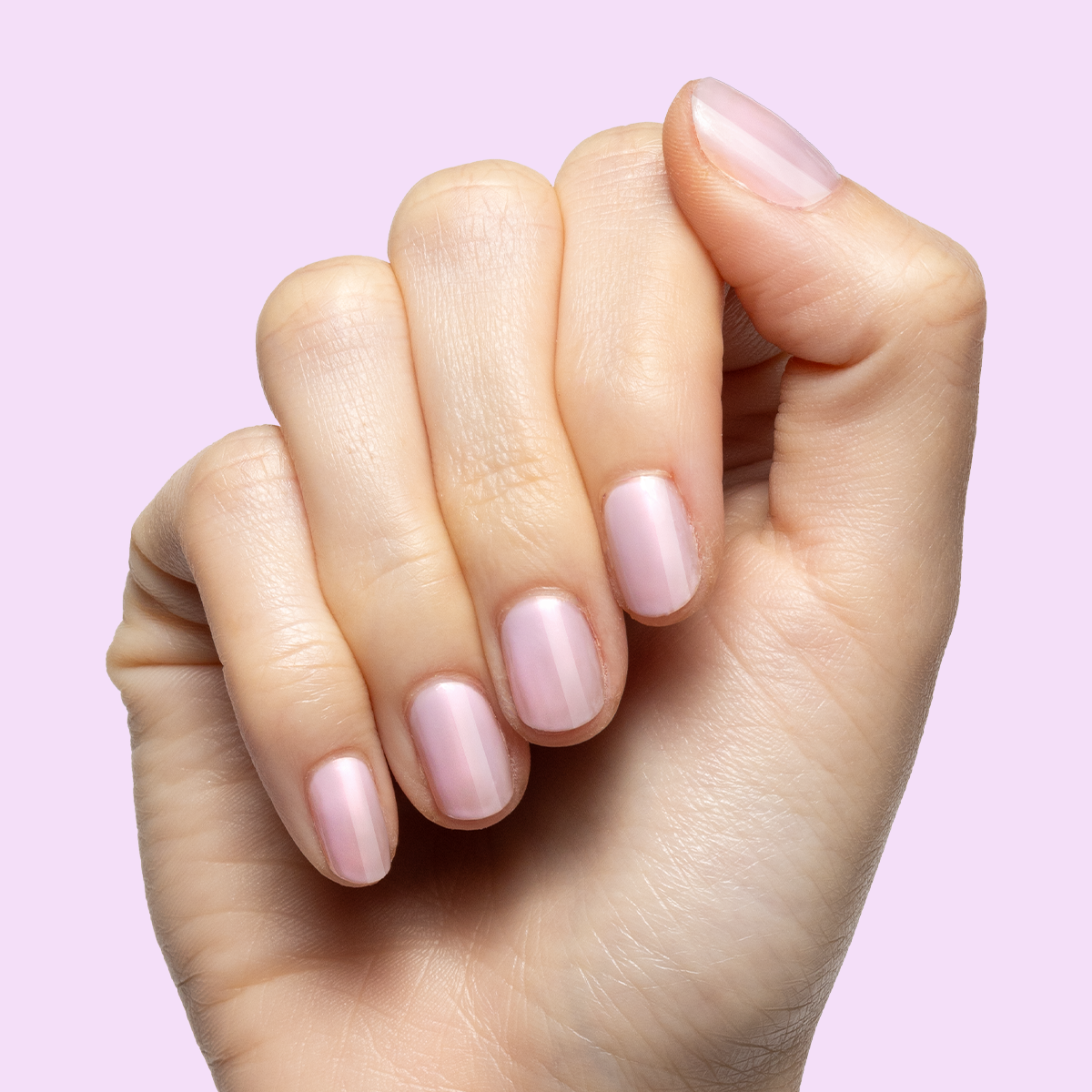 Hand with short natural nails painted in pastel pink using Passionfruit Gloss polish on soft lavender background